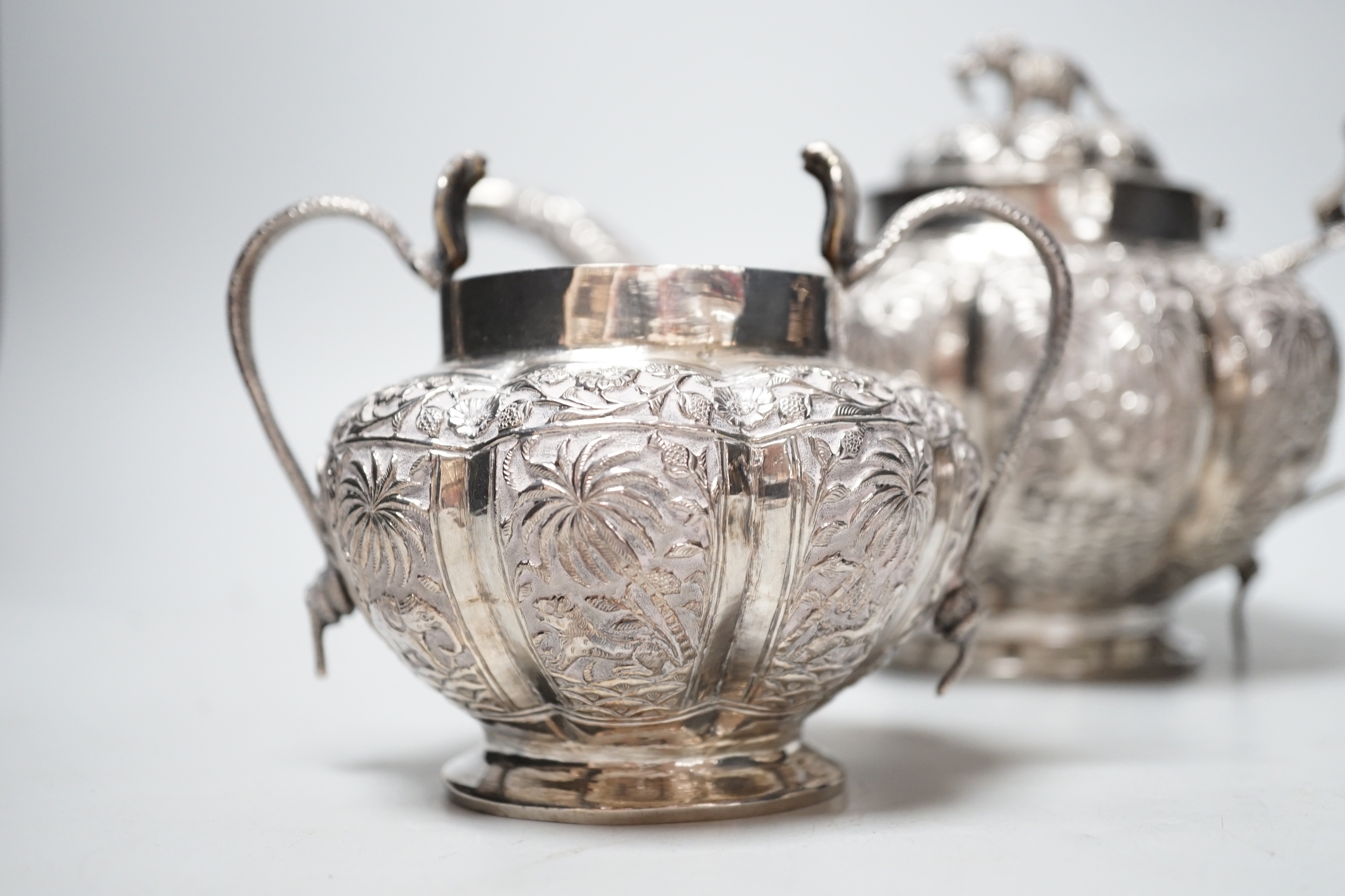 An Indian embossed white metal three piece tea set, with cobra handles and elephant finial, 25.7oz.